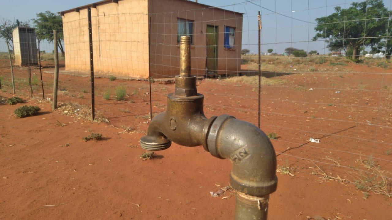 Photo of tap in front of dry soil and building